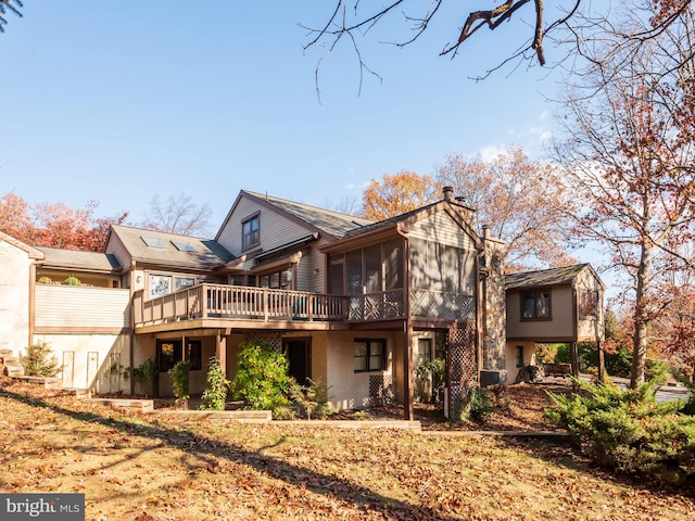 rear view of property with a deck, a sunroom, and a chimney