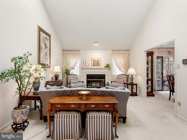 living area with high vaulted ceiling, a glass covered fireplace, light colored carpet, and baseboards