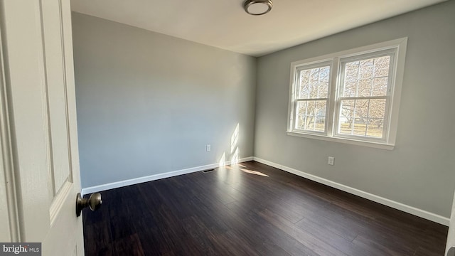 empty room featuring dark wood-style flooring, visible vents, and baseboards