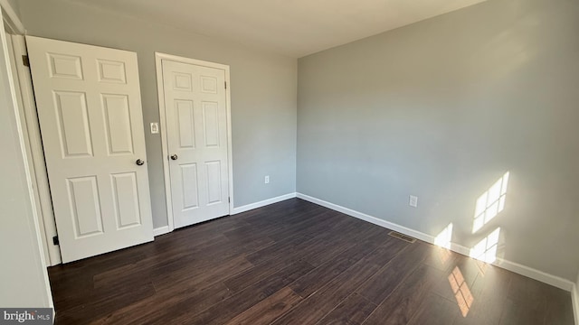 unfurnished bedroom featuring baseboards, visible vents, and dark wood finished floors