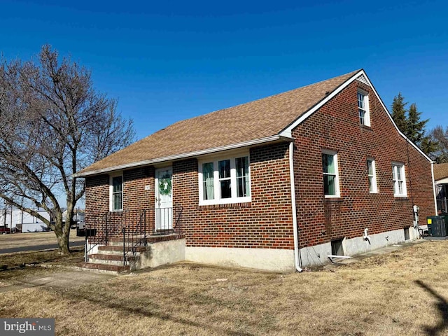 view of front of property with brick siding, central AC, and a front lawn