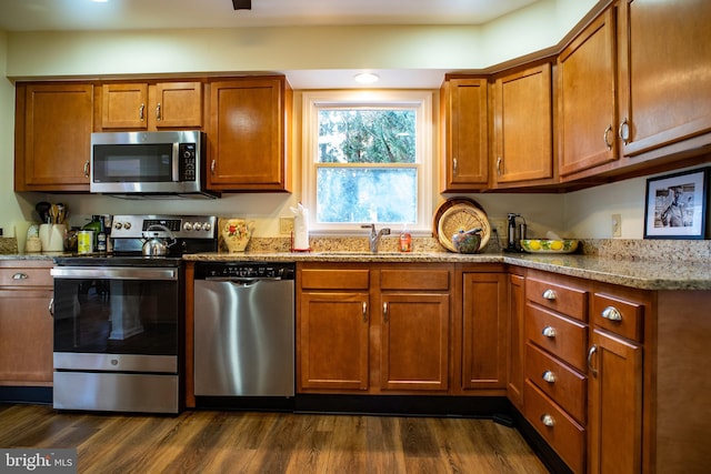 kitchen featuring appliances with stainless steel finishes, brown cabinetry, dark wood finished floors, and a sink