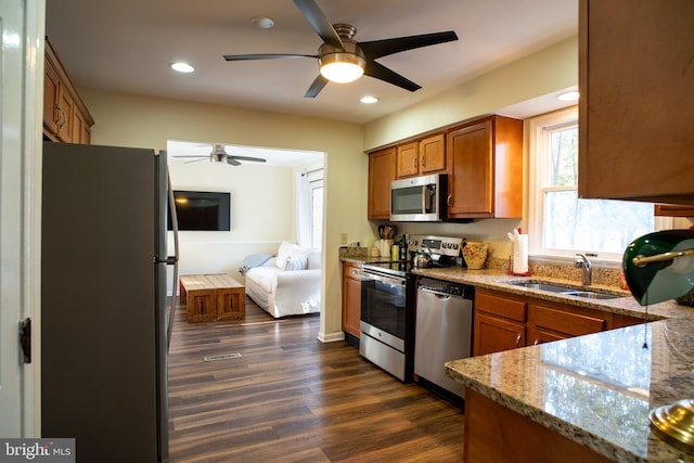 kitchen with a sink, appliances with stainless steel finishes, light stone countertops, brown cabinetry, and dark wood finished floors