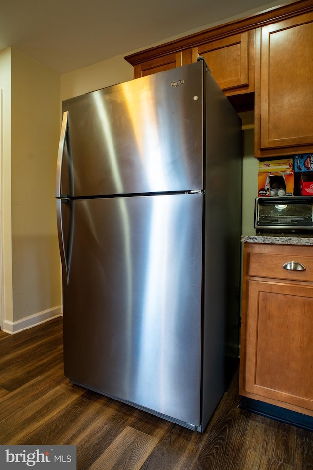 kitchen featuring brown cabinetry, dark wood finished floors, freestanding refrigerator, and baseboards