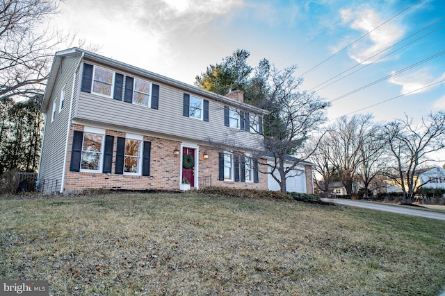 view of front facade with a front yard, brick siding, a chimney, and an attached garage