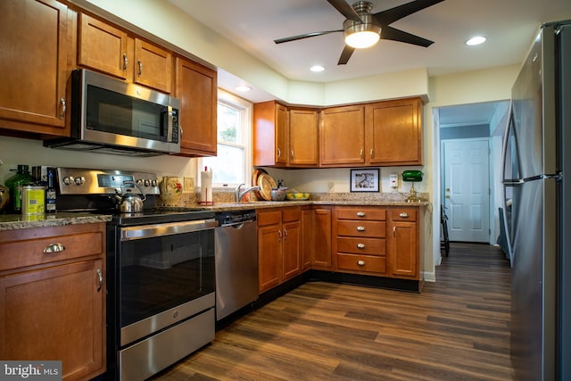 kitchen featuring stone countertops, brown cabinetry, dark wood finished floors, appliances with stainless steel finishes, and recessed lighting