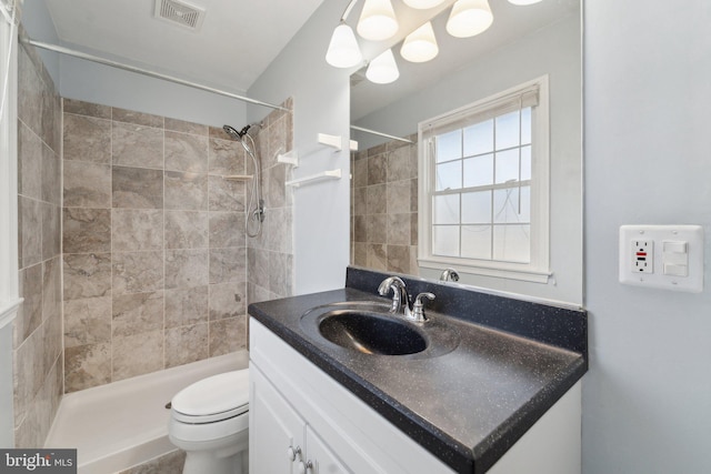 bathroom with toilet, tiled shower, vanity, and visible vents