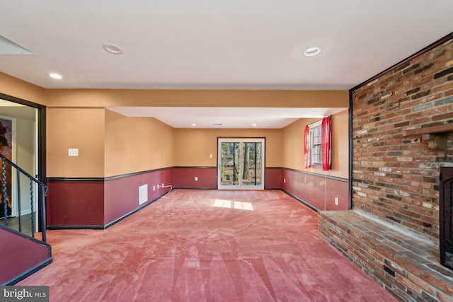 empty room with a brick fireplace, recessed lighting, carpet flooring, and wainscoting