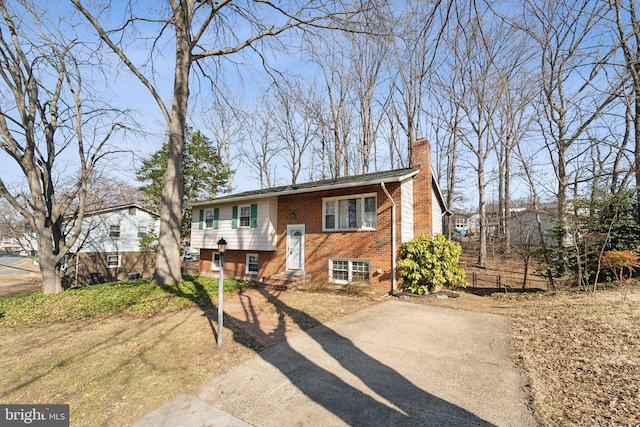 bi-level home with driveway, brick siding, a chimney, and fence