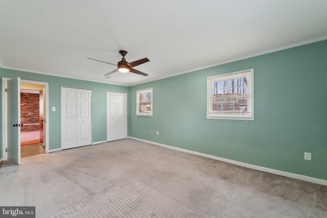 unfurnished bedroom featuring ceiling fan, baseboards, multiple closets, carpet, and crown molding