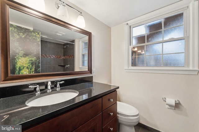 bathroom featuring a tile shower, vanity, and toilet