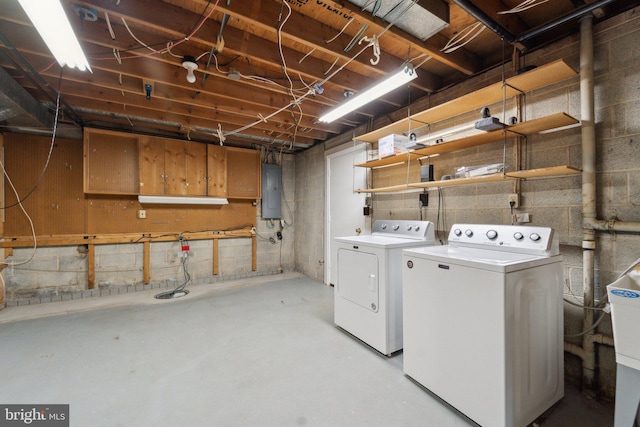 clothes washing area featuring concrete block wall, laundry area, electric panel, and washing machine and clothes dryer