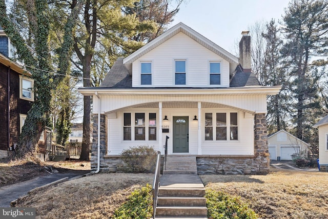 view of front of house with a shingled roof, a chimney, a detached garage, an outdoor structure, and a porch