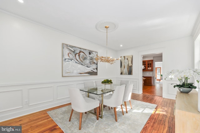 dining space featuring light wood finished floors, a chandelier, and a decorative wall