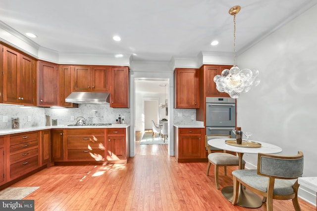 kitchen featuring under cabinet range hood, light countertops, appliances with stainless steel finishes, light wood finished floors, and decorative light fixtures