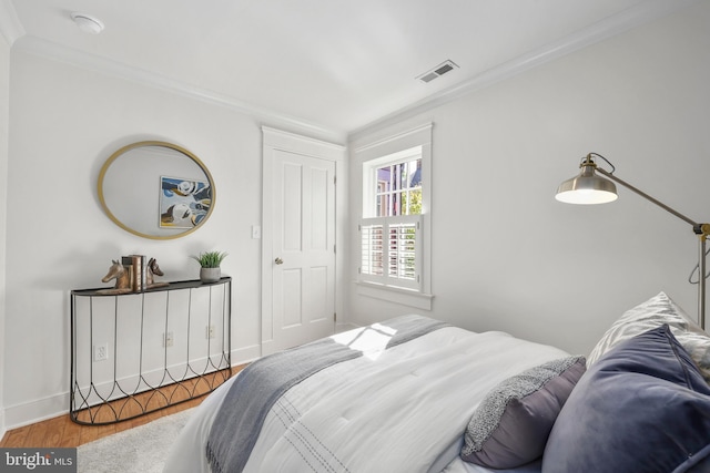 bedroom with baseboards, wood finished floors, visible vents, and crown molding