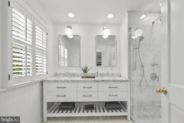 full bath with double vanity, a marble finish shower, and a sink