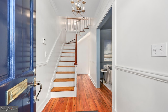 entrance foyer featuring baseboards, hardwood / wood-style floors, an inviting chandelier, stairs, and crown molding