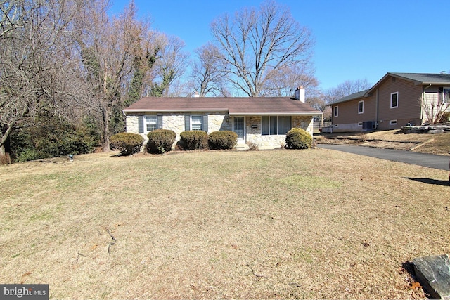 single story home featuring stone siding, a chimney, and a front lawn