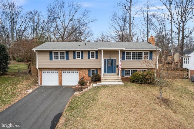 bi-level home with brick siding, a chimney, aphalt driveway, an attached garage, and a front yard