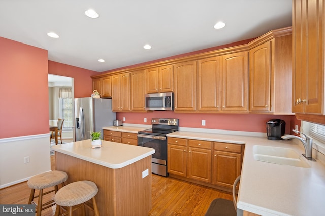 kitchen with a sink, a breakfast bar, stainless steel appliances, light countertops, and a center island