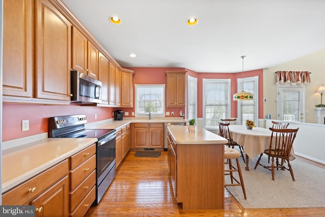 kitchen featuring a kitchen breakfast bar, a sink, appliances with stainless steel finishes, light countertops, and a kitchen island