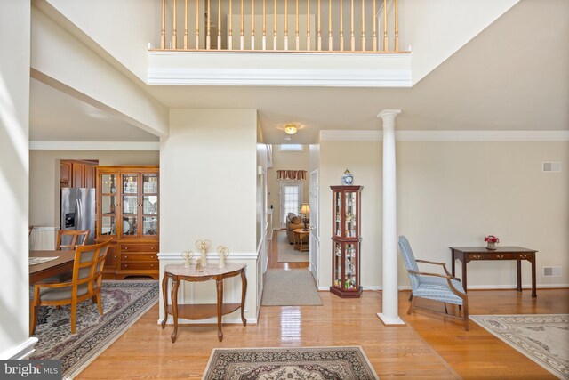 foyer with a towering ceiling, visible vents, light wood-style floors, and ornate columns