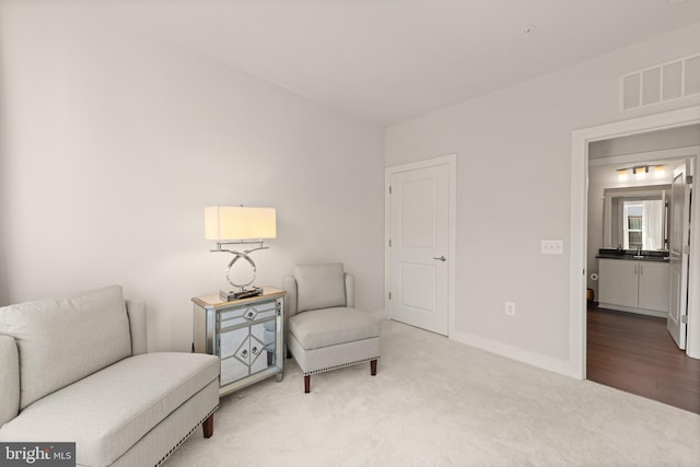 sitting room with baseboards, visible vents, and light colored carpet