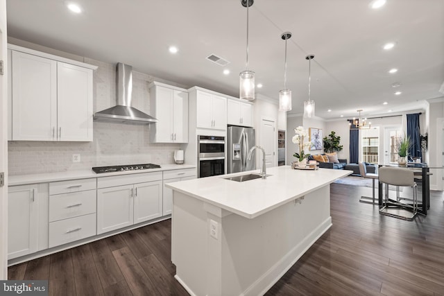 kitchen with visible vents, white cabinetry, a sink, wall chimney range hood, and a kitchen island with sink