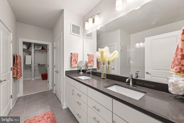 bathroom with double vanity, tile patterned flooring, a tile shower, and a sink