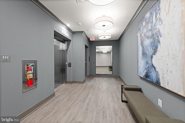 corridor with crown molding, visible vents, light wood-style flooring, elevator, and baseboards