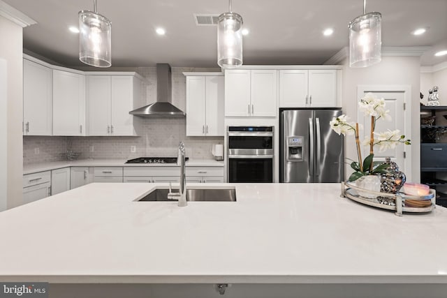 kitchen featuring stainless steel appliances, light countertops, white cabinetry, a sink, and wall chimney range hood