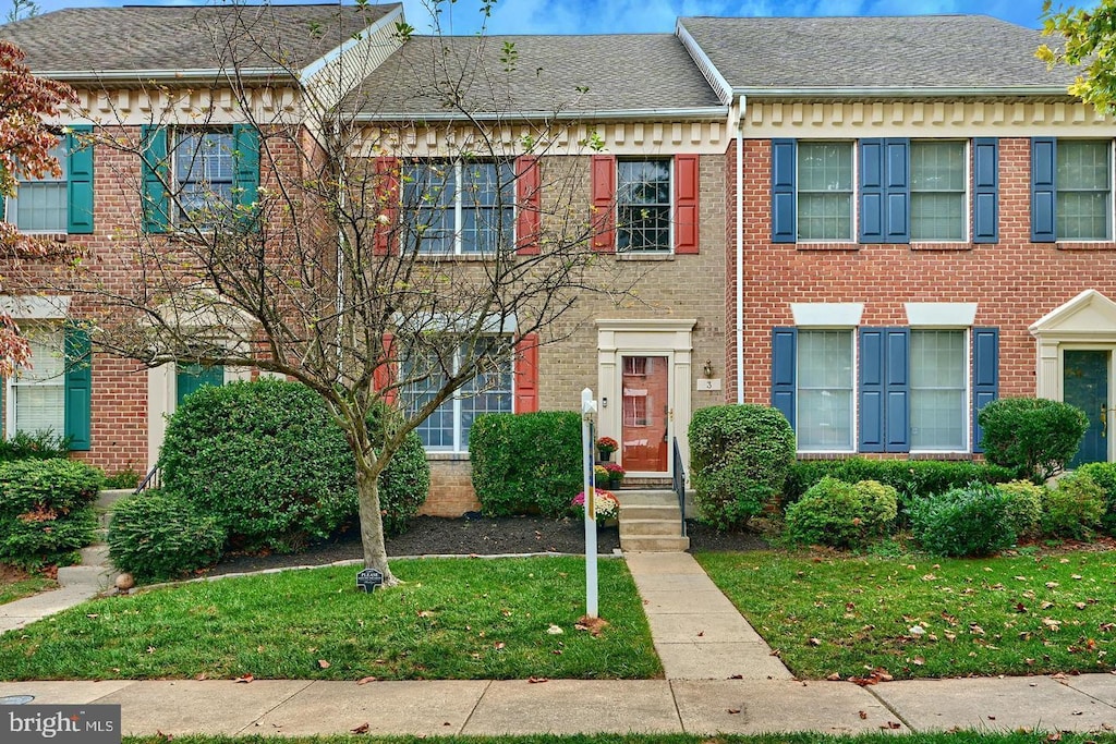 townhome / multi-family property featuring brick siding, a front lawn, and a shingled roof