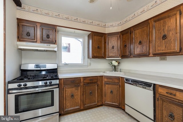 kitchen featuring white dishwasher, under cabinet range hood, light floors, stainless steel range with gas stovetop, and wallpapered walls