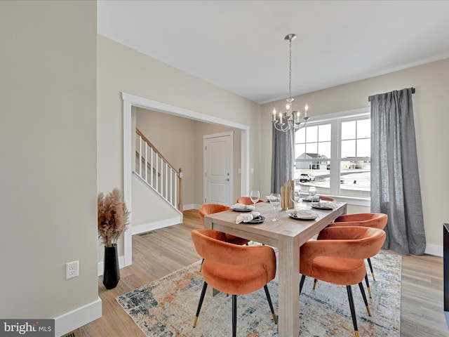 dining area with visible vents, baseboards, light wood-style flooring, stairway, and an inviting chandelier