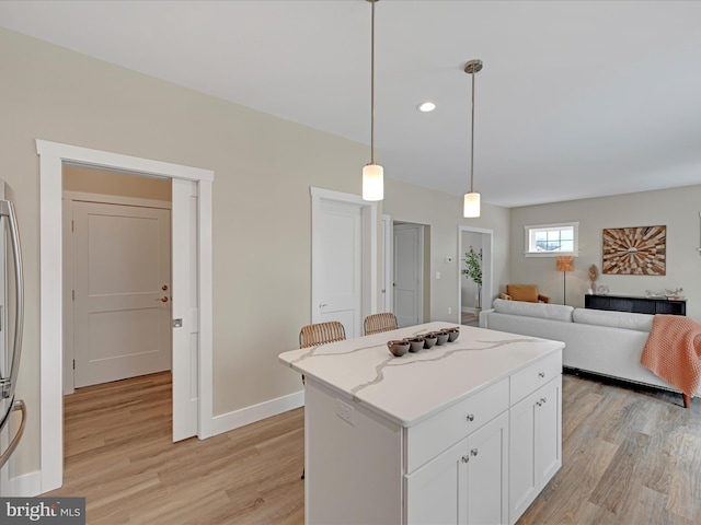 kitchen featuring light wood-style flooring, a kitchen island, decorative light fixtures, and white cabinets