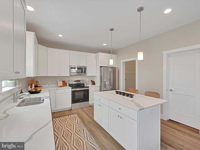 kitchen with light stone counters, stainless steel appliances, white cabinets, a sink, and a kitchen island