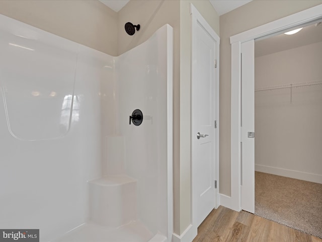 full bath with a walk in closet, walk in shower, baseboards, and wood finished floors