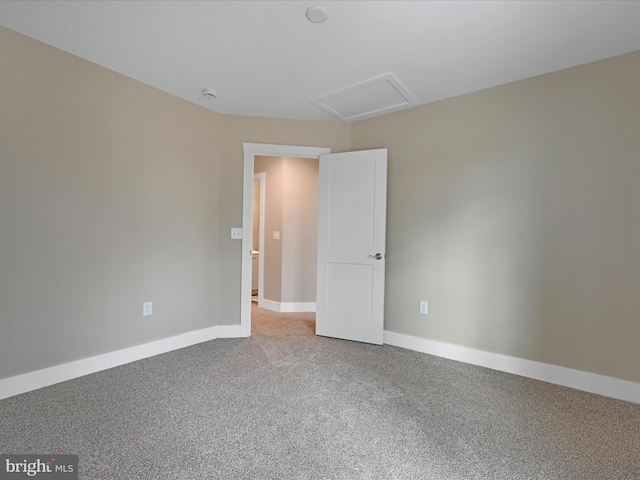 carpeted empty room with attic access and baseboards