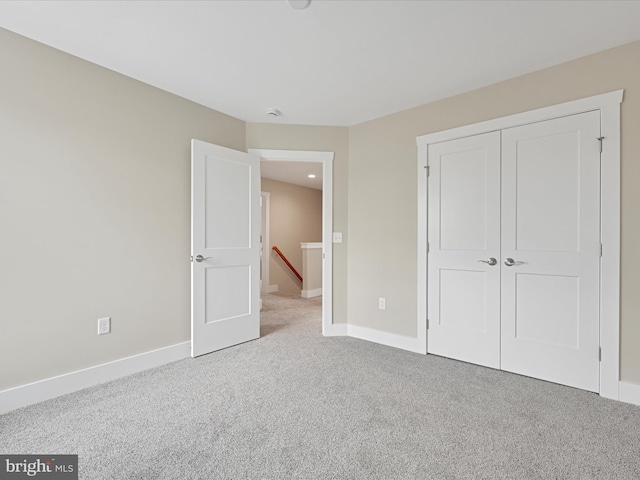 unfurnished bedroom with a closet, light carpet, and baseboards