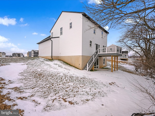 snow covered rear of property with stairs and a wooden deck