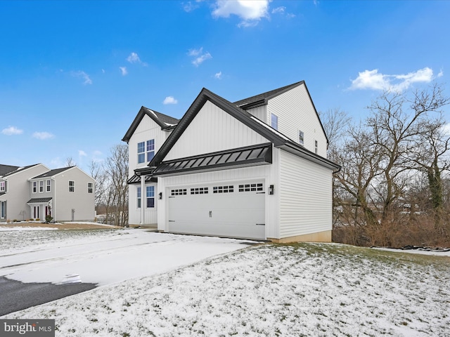 view of snowy exterior featuring board and batten siding, a standing seam roof, metal roof, and an attached garage