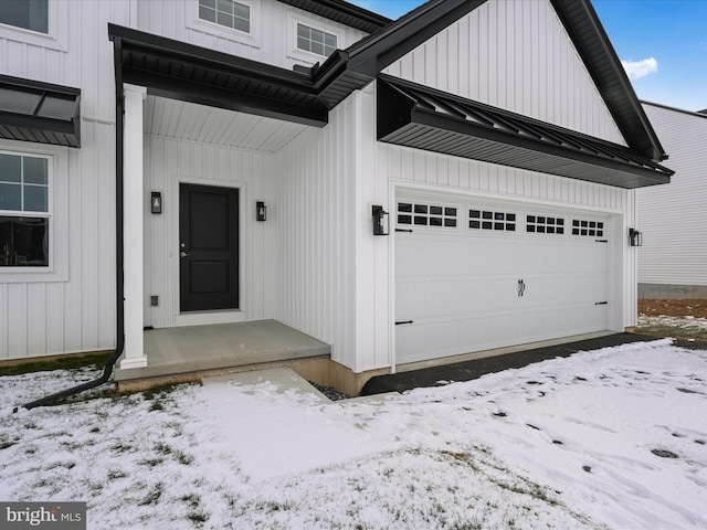 snow covered property entrance with a garage, a standing seam roof, metal roof, and board and batten siding