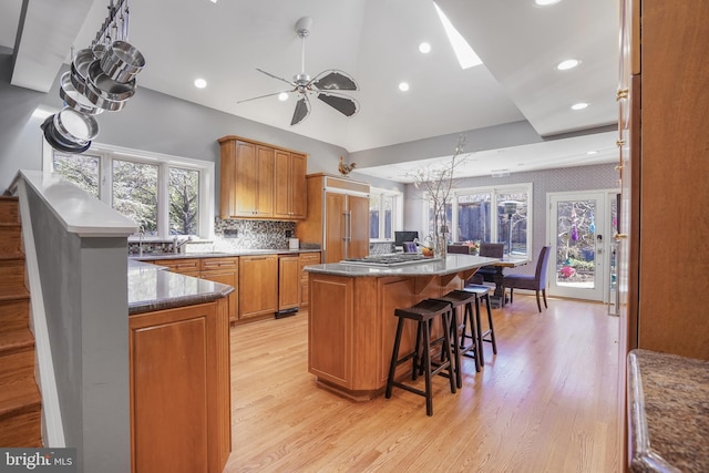 kitchen featuring a kitchen island, a ceiling fan, a kitchen breakfast bar, light wood-style floors, and brown cabinetry