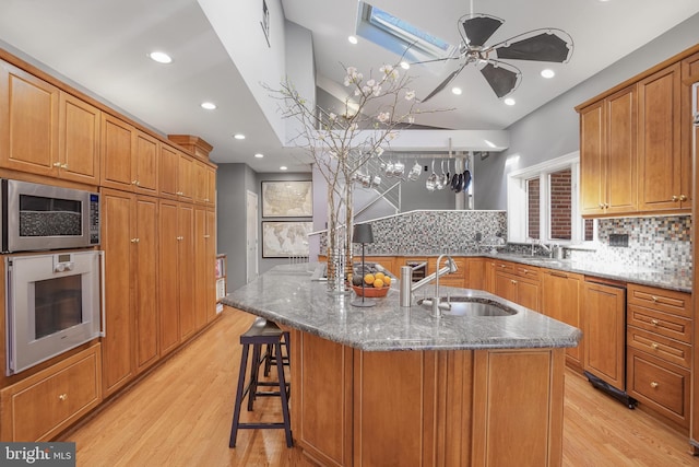 kitchen with stone countertops, oven, stainless steel microwave, a sink, and brown cabinetry