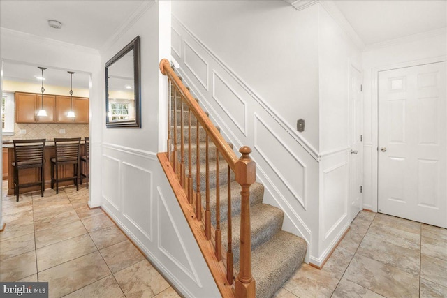 staircase featuring a decorative wall, crown molding, and wainscoting