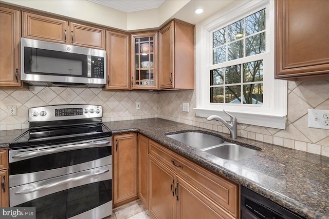 kitchen with stainless steel appliances, dark stone counters, brown cabinetry, and a sink