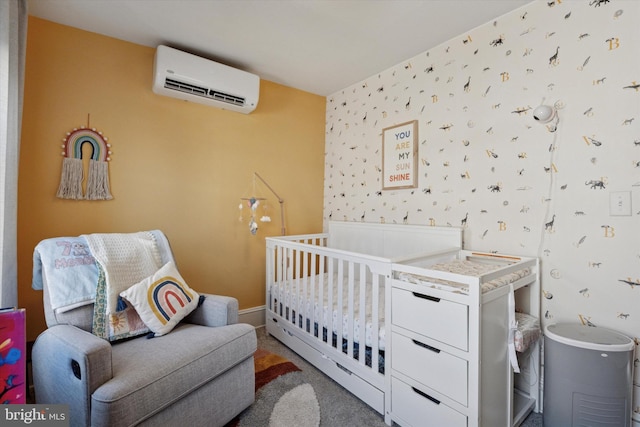 carpeted bedroom with wallpapered walls, baseboards, a nursery area, and a wall mounted AC