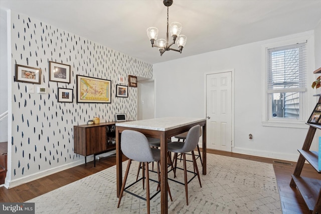 dining space featuring wallpapered walls, baseboards, an accent wall, wood finished floors, and a notable chandelier