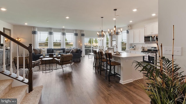 kitchen with a center island with sink, white cabinets, appliances with stainless steel finishes, open floor plan, and decorative light fixtures